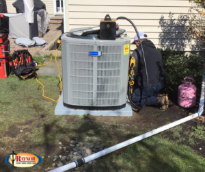 An outdoor HVAC unit being serviced by a Raynor Services technician